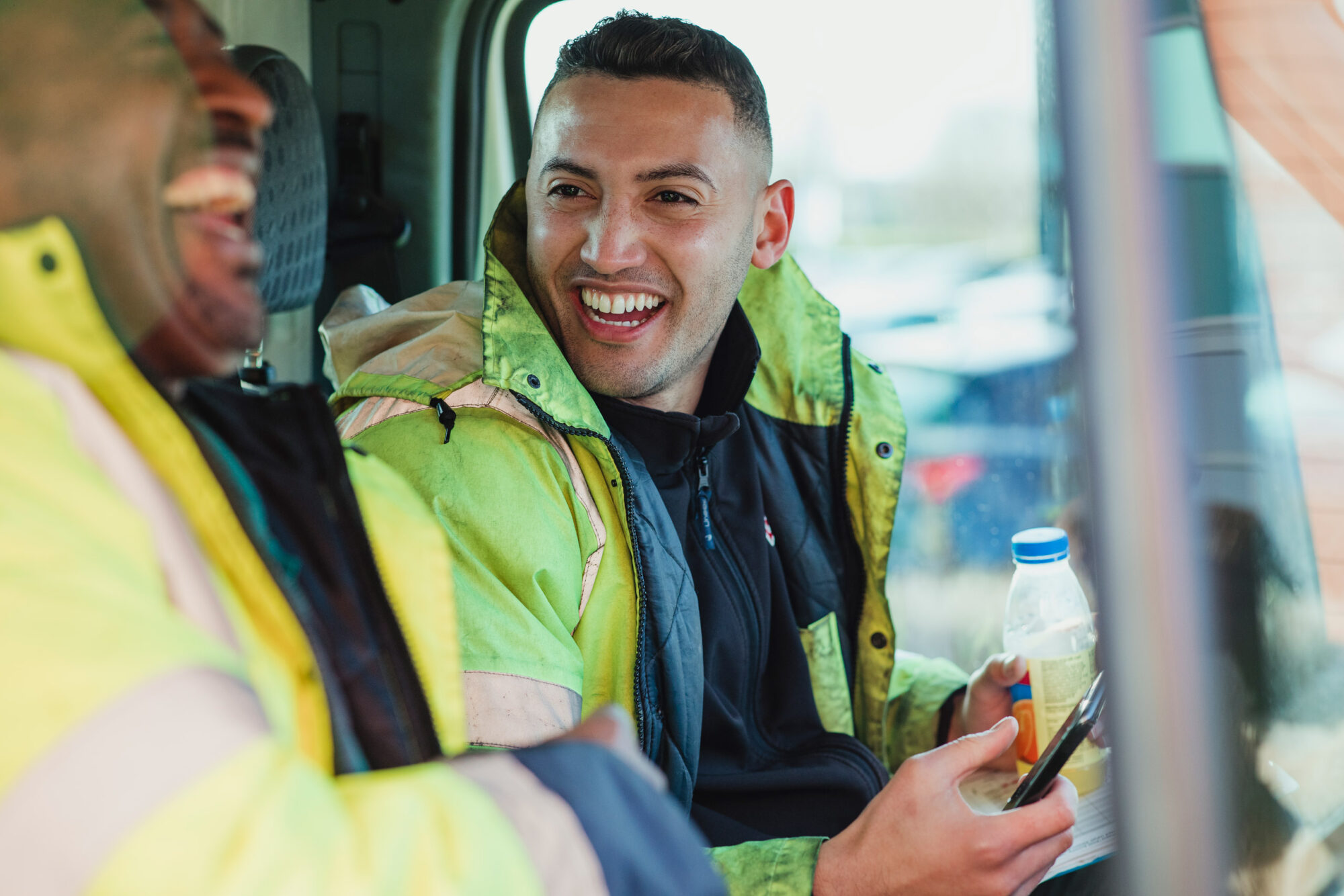 Two men, in high vis jackets laughing in a van